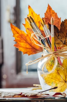 Closeup of artist paint brushes and autumn maple leaves in art studio.