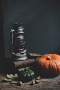 Still life with old lantern, halloween pumpkin and autumn decoration on rustic wooden table. Thanksgiving and Halloween holiday concept with copyspace.