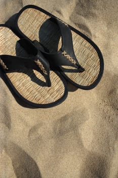 An image of sandals resting on the hot sand of a tropical beach.
