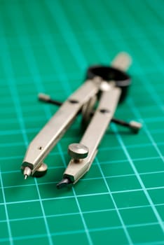 pair of spring-bow compasses on green cutting mat  differential focus  selective lighting