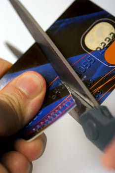 Macro image of scissors cutting through a credit card.  Logos are fake and numbers have been changed.  Colours of the card have been altered also.