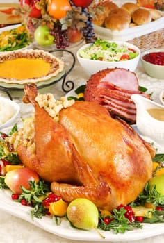 Thanksgiving dinner with roast turkey, baked ham, pumpkin pie, gravy, dinner rolls, cranberry chutney etc.