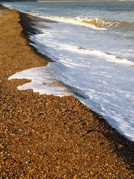 Gentle waves break on a pebble beach at Dunwich in the UK.