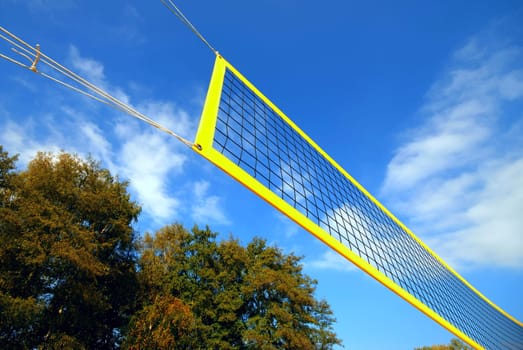 yellow volleyball net under blue clouded sky, in the background autumn trees