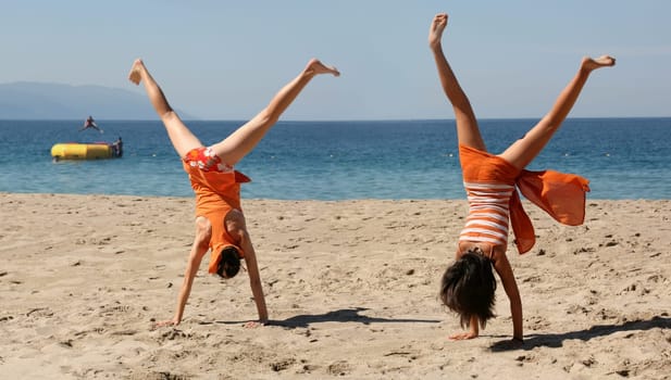 Two girls in orange clothes doing cartwheel on the beach