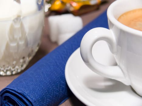 A cup of coffee with foam, milk, sugar and a blue napkin