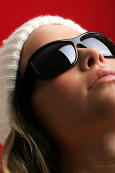 portrait of a beautiful woman with a cap and some sunglasses against red background