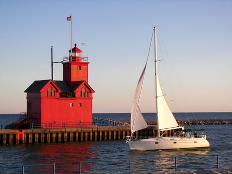 Sailboat passing a red lighthouse in the harbor.