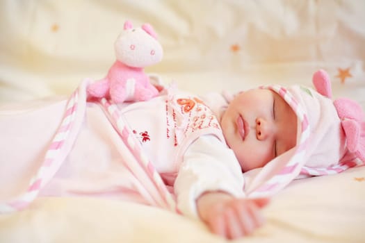 Lying sleeping baby with small teddy bear on bright background