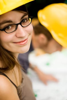 young female smiling architect or builder wearing a yellow hart hat on a construction site