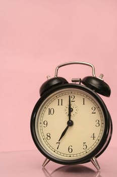 The black alarm clock is on a pink background