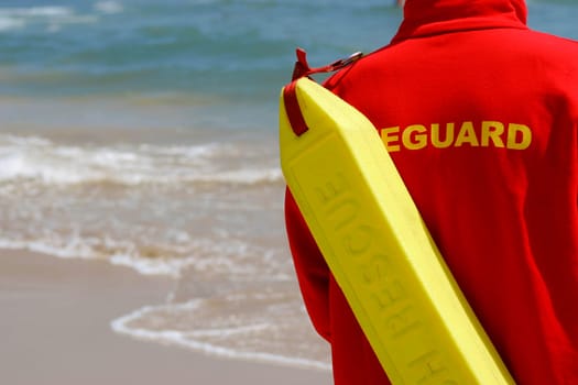 A lifeguard with float surveys a wave swept beach