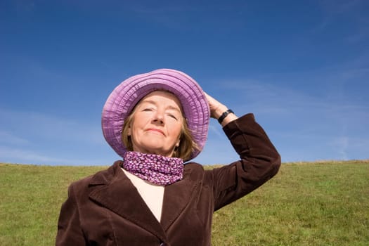 Happy mature woman on the meadow - in her favourite violet hat :-)