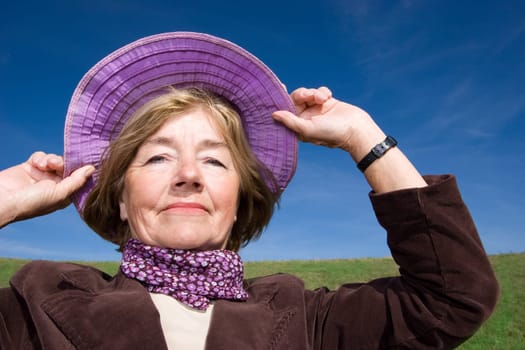 Happy mature woman on the meadow - in her favourite violet hat :-)
