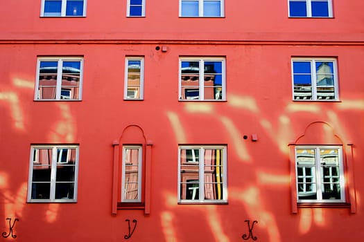 Oslo, Norway. Reflections in the windows of a building painted with strong color, reflections of the sunlight on the facade.