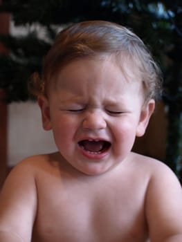 upset baby boy screaming in front of christmas tree