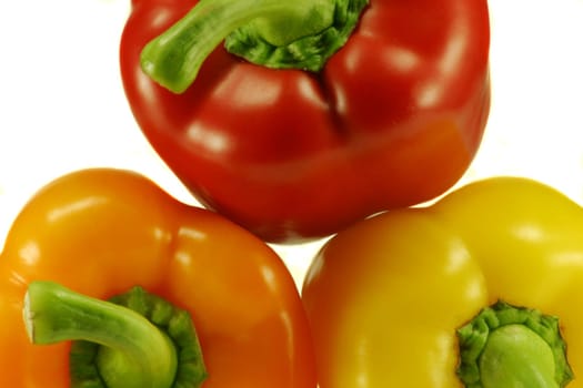 Macro view of red, yellow and orange peppers stacked, on white background