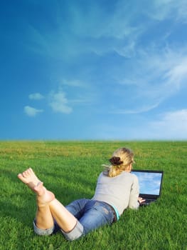 A girl using a laptop in a field.