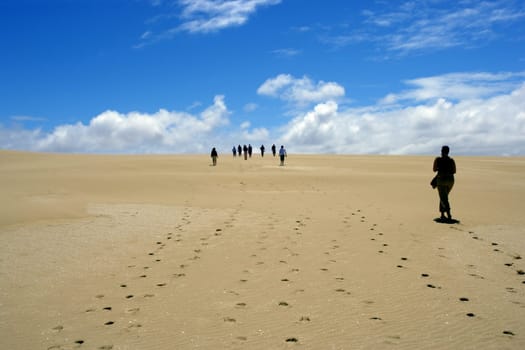 Group of people walking on sand dunes.