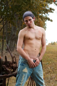 Fit shirtless male artist with tattoo and jeans on a farm