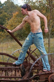 Fit shirtless male artist with tattoo and jeans on a farm