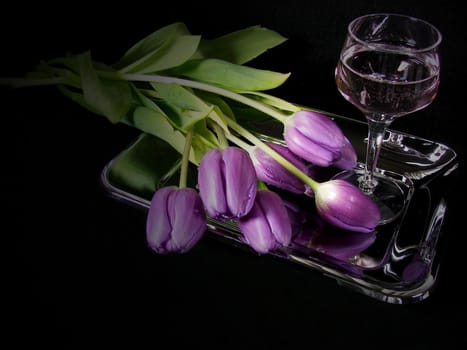 Bouquet of purple tulips on a silver plate with a glass of wine.