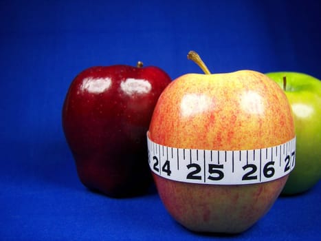 Various kinds of apples on blue background with tape measure.