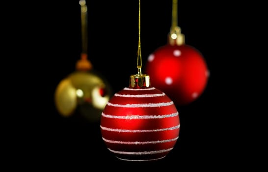 Three hanging Christmas baubles isolated on a black background
