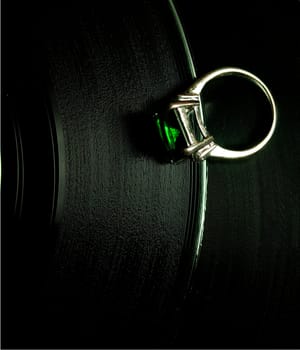 a white gold ring with a green stone lying on a vinyl disc