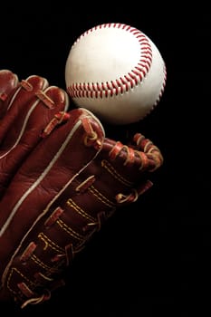 Close up of a baseball glove and a ball on a black background