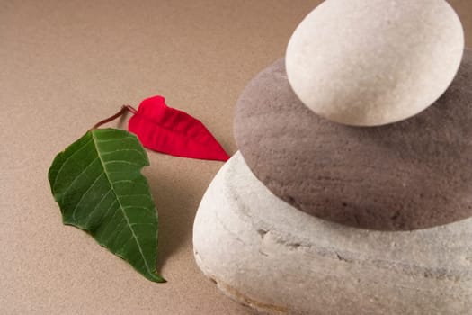 3 balanced pebbles with red and green leaves on a clear background