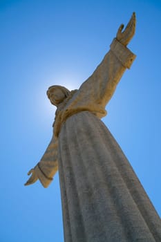 Huge Jesus Christ statue with arms outstretched, sun behind head and blue sky