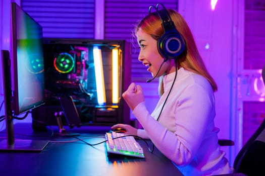 Winning Victory. Asian gamer playing online video game excited on desktop computer PC colorful neon LED lights, woman in gaming headphones use computer she happy successful, E-Sport concept, side view