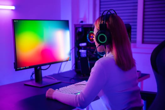 Asian professional gamer playing online video game on desktop computer PC have colorful neon LED lights, young woman in gaming headphones using computer for playing game at home