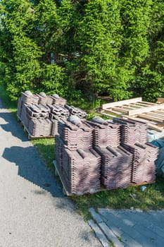 Old dismantled roof shingles after replacement neatly stacked on pallets in sunny side light with shadows.