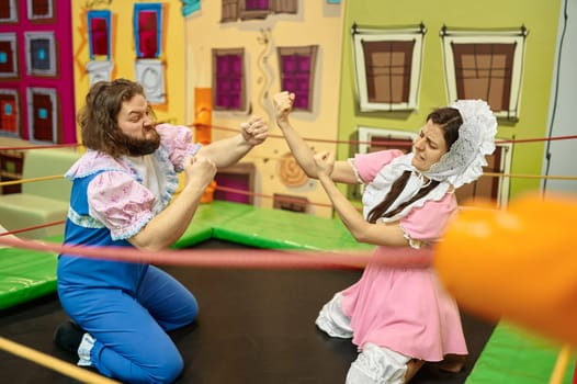 Funny excited man and woman wearing like babies boxing on toy ring in indoor playroom