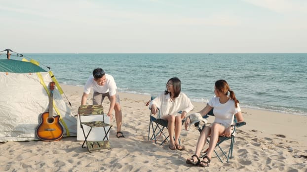 Happy friends with drinks in camp and laughing together in holidays on sand beach near camping tent vacation time at sunset, Young Asian group woman and man in summer travel outdoor