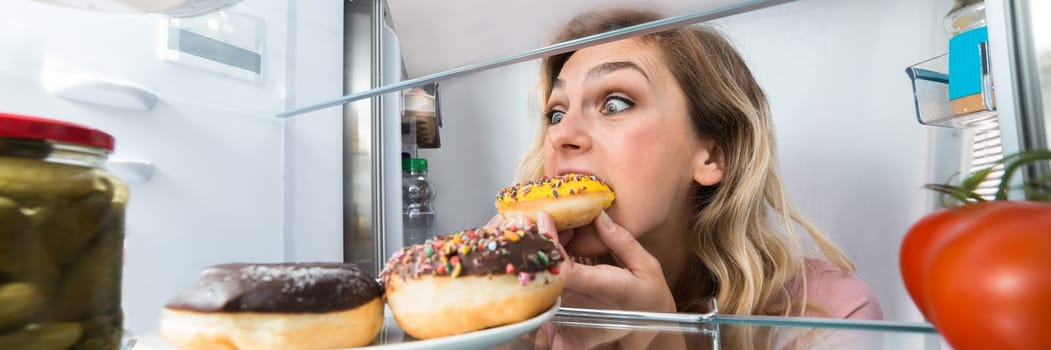 Young Happy Woman Eating Donut From Refrigerator