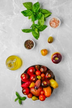 Vertical composition with various types of tomatoes, basil and spice on marble background