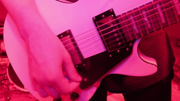 Repetition of rock music band. Cropped image of electric guitar player in a red light.