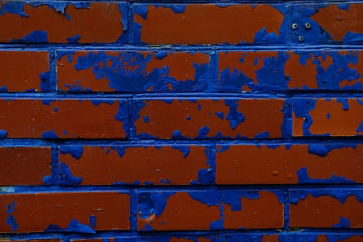 Colorful wall background with damaged paints of blue on red bricks.