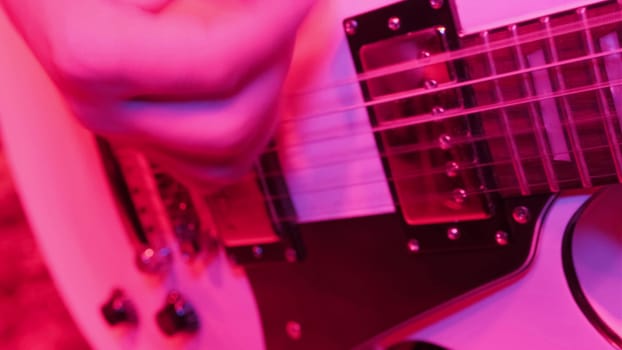 Repetition of rock music band. Cropped image of electric guitar player in a red light.