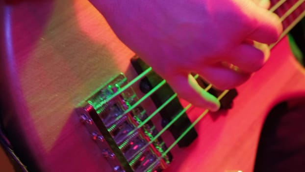 Hands of rock musician playing the electric bass guitar on repetitin in red light.