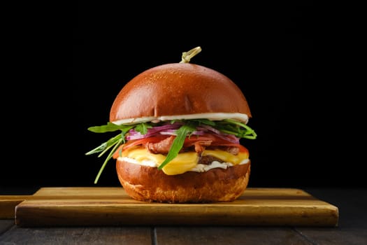 Burger with beef and crispy bacon on wooden serving board over black background