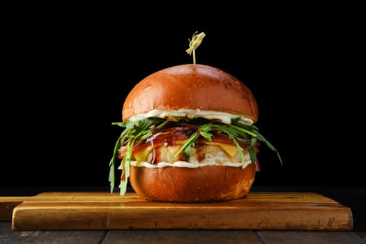 Burger with chicken patty teriyaki sauce on wooden serving board over black background
