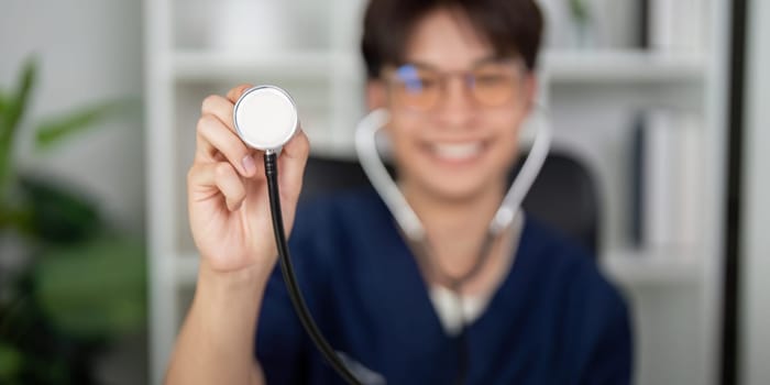A cheerful medical student in scrubs holds up a stethoscope, showcasing excitement for a career in healthcare and patient interaction.