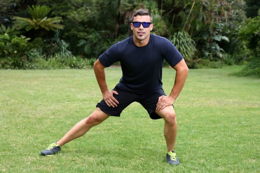 Handsome young man doing stretching exercises outdoors
