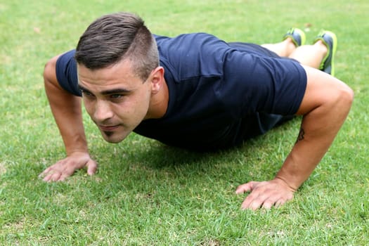 Handsome young man doing pushup exercises outdoors