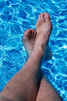 Feet and legs cooling off in sparkling blue pool water