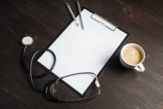 Various medical supplies. Blank medical clipboard, stethoscope, coffee cup, thermometer and pen on wooden background.